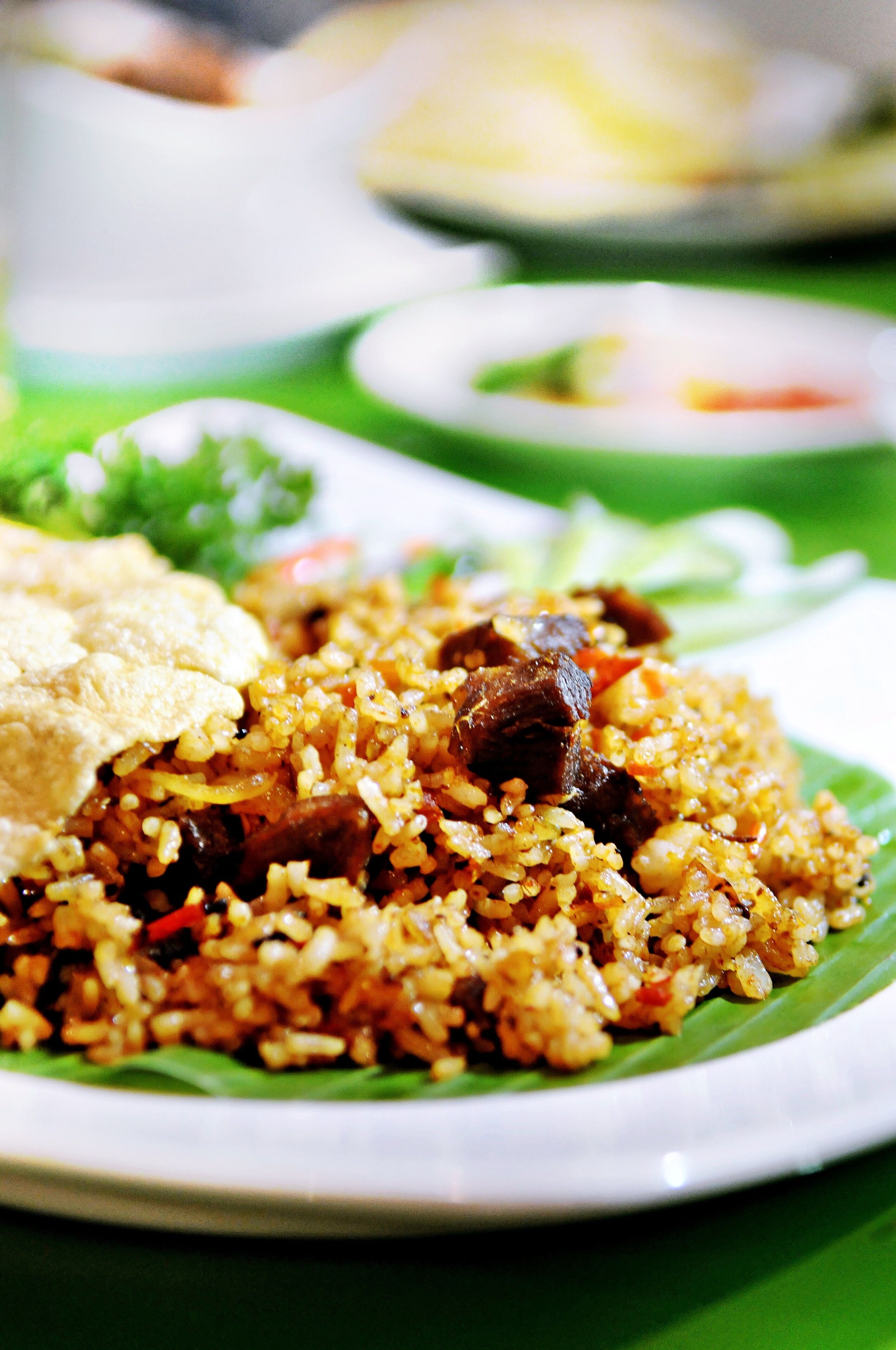 A plate of fried rice with vegetables and meat, served on a green leaf.
