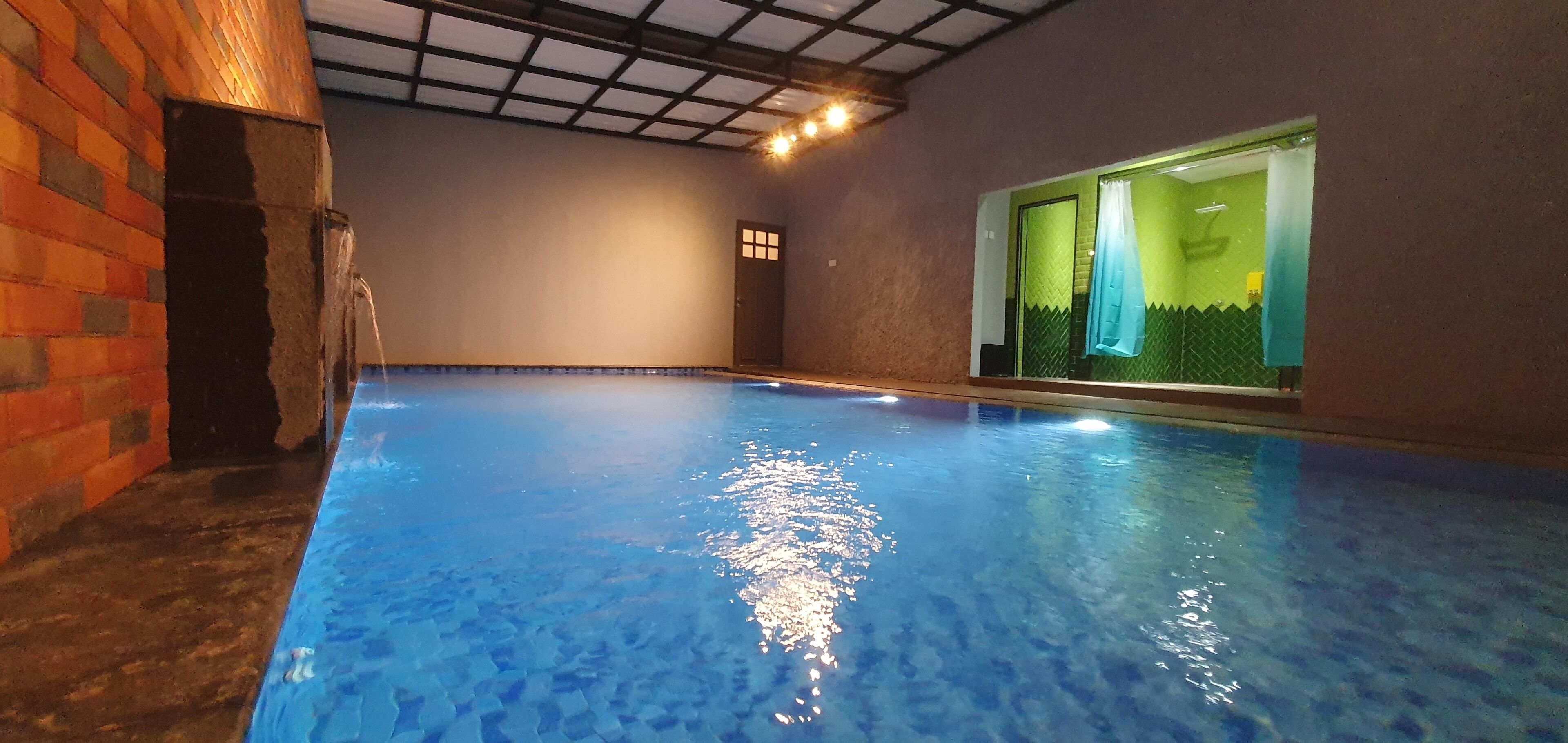 An indoor swimming pool with clear water, a brick wall on one side, and a door leading to a room with a green and white color scheme.