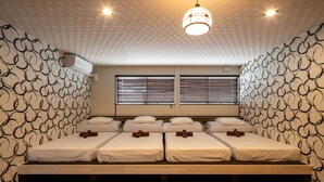 Una habitación de hotel con cuatro camas individuales, un ventanal con persianas, un papel tapiz decorativo y una lámpara colgante.