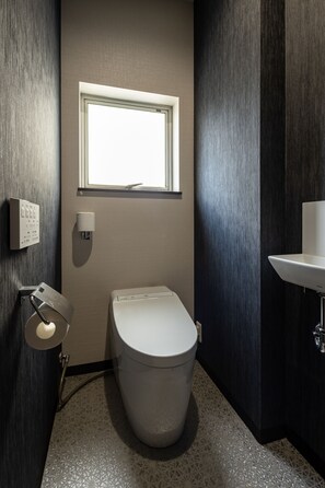 Un baño moderno con inodoro, ventana, luz empotrada y lavamanos.
