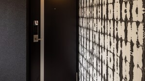 Un pasillo con un papel tapiz estampado, una puerta con una franja vertical y un accesorio de iluminación encima.