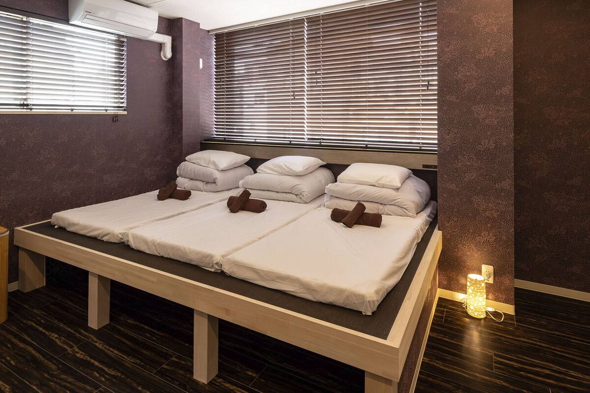A double bed with white linens and brown towels, a wooden bedside table, and a small bedside lamp.