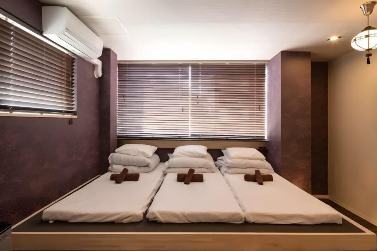 A room with a bed, a window with blinds, and a ceiling light fixture.