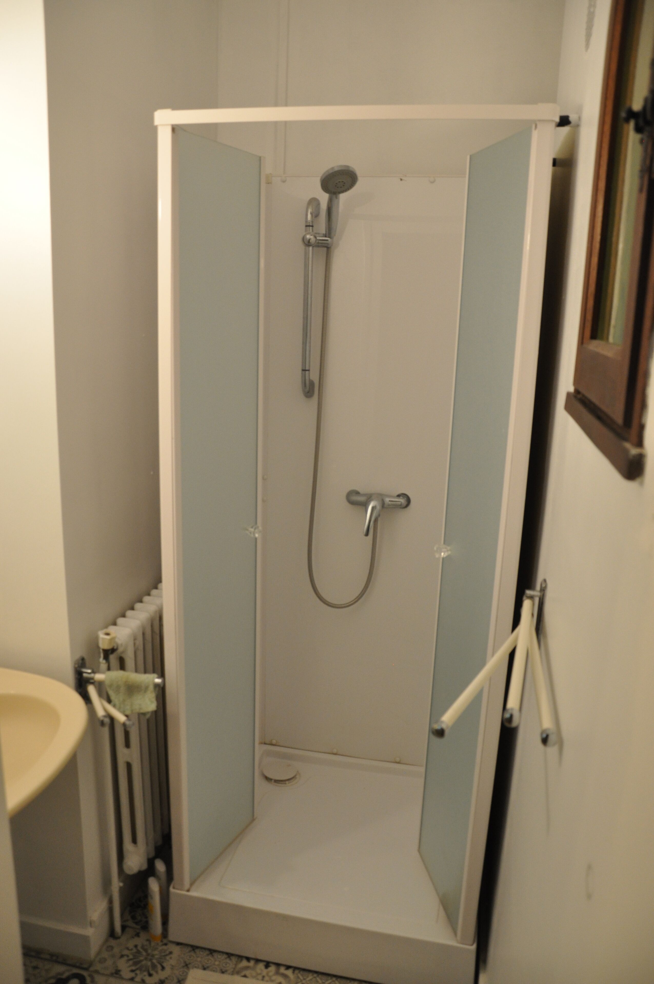A small, enclosed shower area with a showerhead and faucet, adjacent to a toilet and sink.