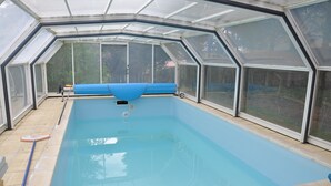 Ein Schwimmbad mit Glasdach und blauer Abdeckung.