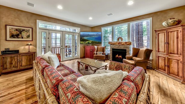 A spacious living room with a large sofa, a fireplace, and a view of a lake through large windows.