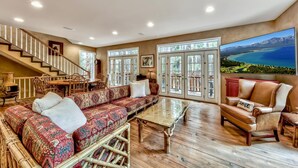 A spacious living room with a large sofa, a glass coffee table, and a leather armchair. A staircase with white railings leads to an upper level.