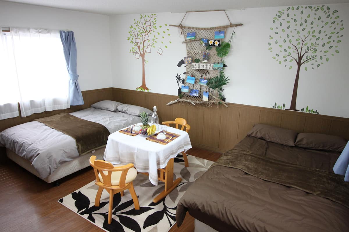Una habitación con dos camas, una mesa de comedor con sillas y un mural de un árbol en la pared.