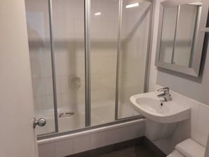 A bathroom with a glass shower enclosure, a white sink, and a toilet.