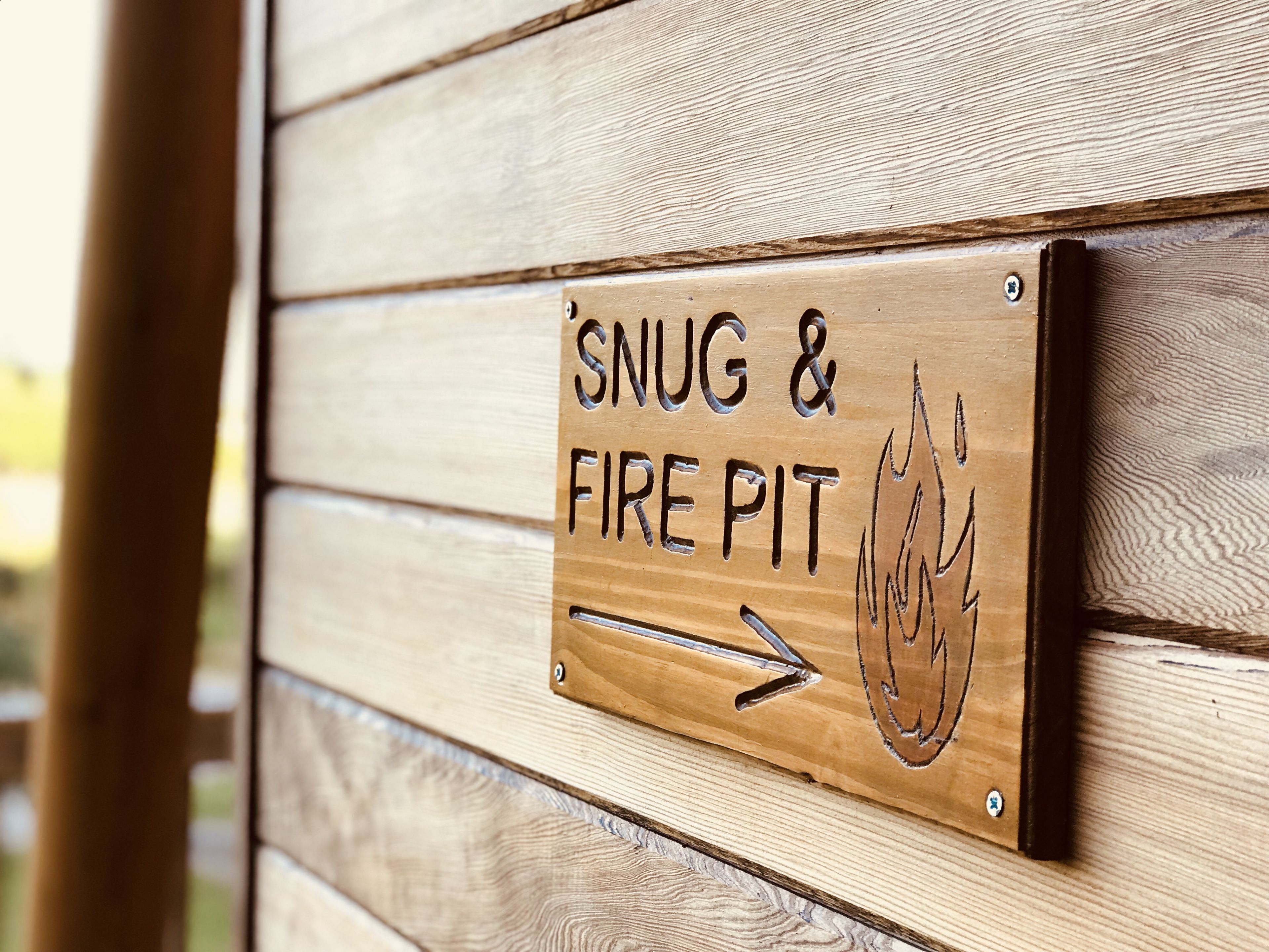 Un panneau en bois portant l’inscription « SNUG & FIRE PIT » et une flèche pointant vers la droite.