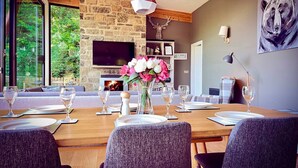 A modern dining room with a stone fireplace, a television, and a large window overlooking greenery. - A yorkshire dale that sleeps 6 guests  in 3 bedrooms (Richmond)