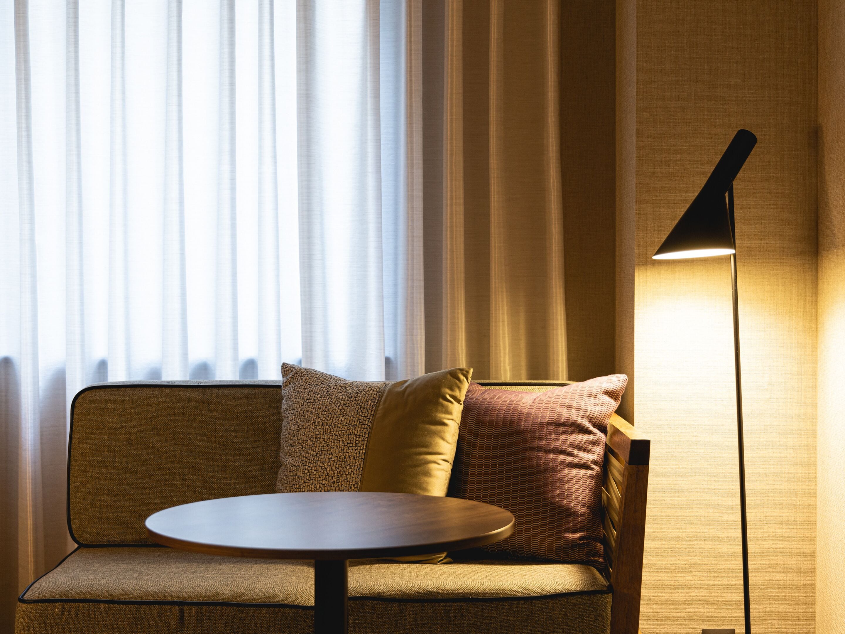 Un espace salon moderne avec une table ronde, un canapé agrémenté de coussins à motifs et un lampadaire.