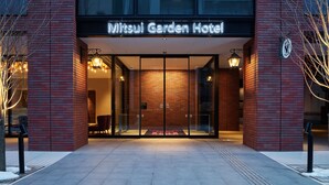 The Mitsui Garden Hotel entrance with glass doors, a brick facade, and a sign above.