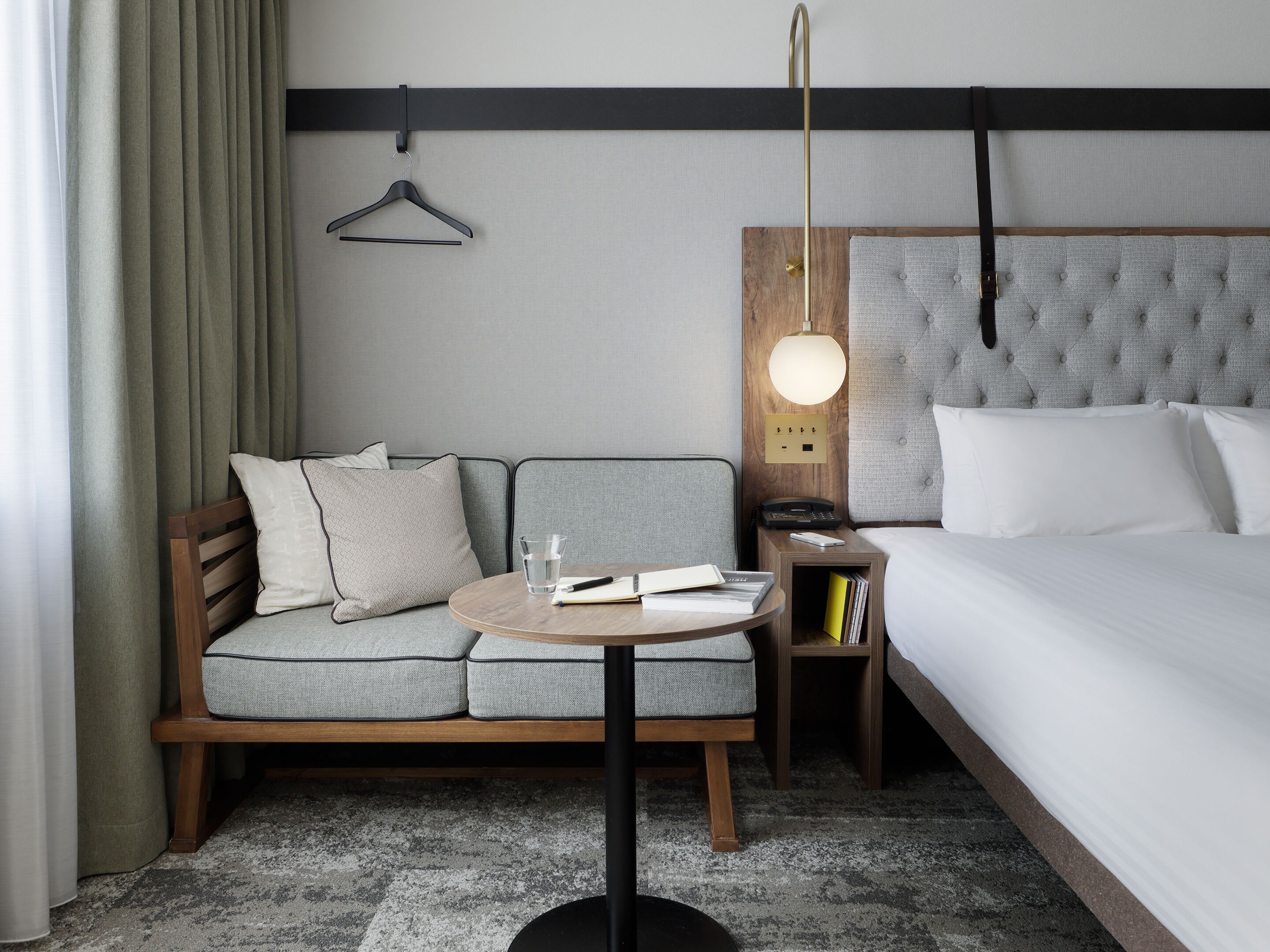 A hotel room with a bed, a sofa, a bedside table, a lamp, and a small nightstand.