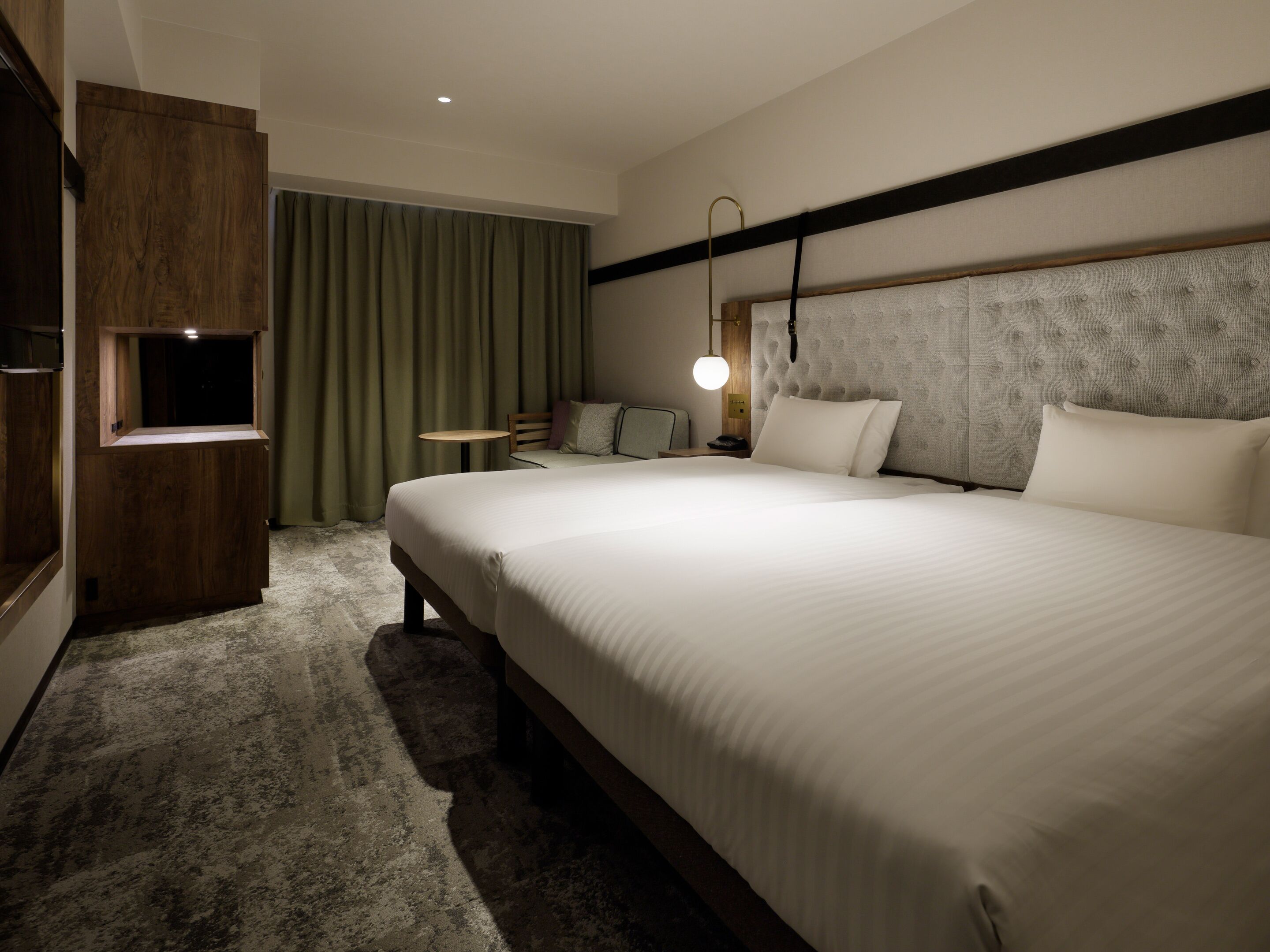A hotel room with a large bed, a wooden wardrobe, a small table, a chair, and a lamp.
