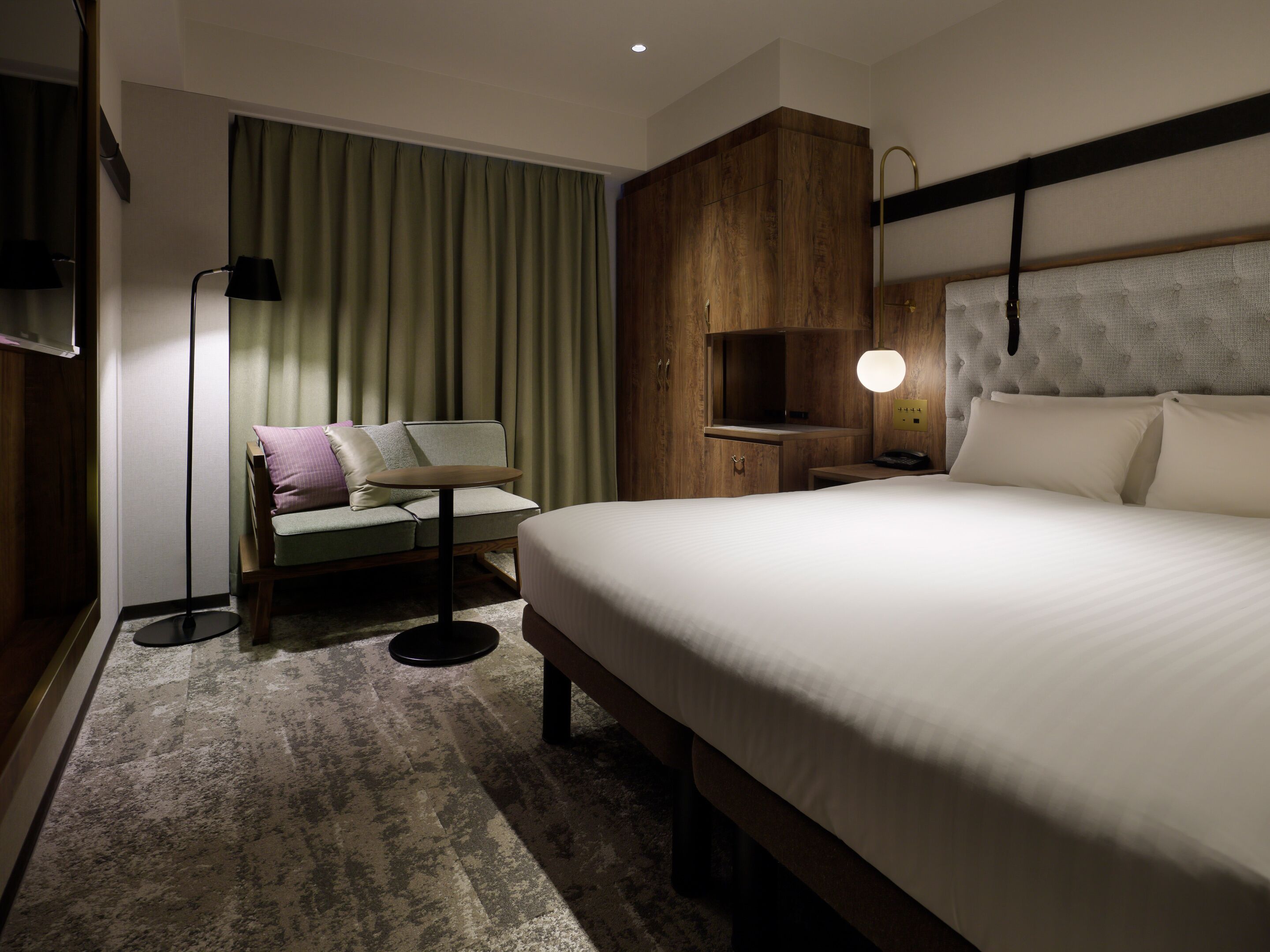 A hotel room with a bed, a sofa, a desk, a lamp, and a wardrobe.
