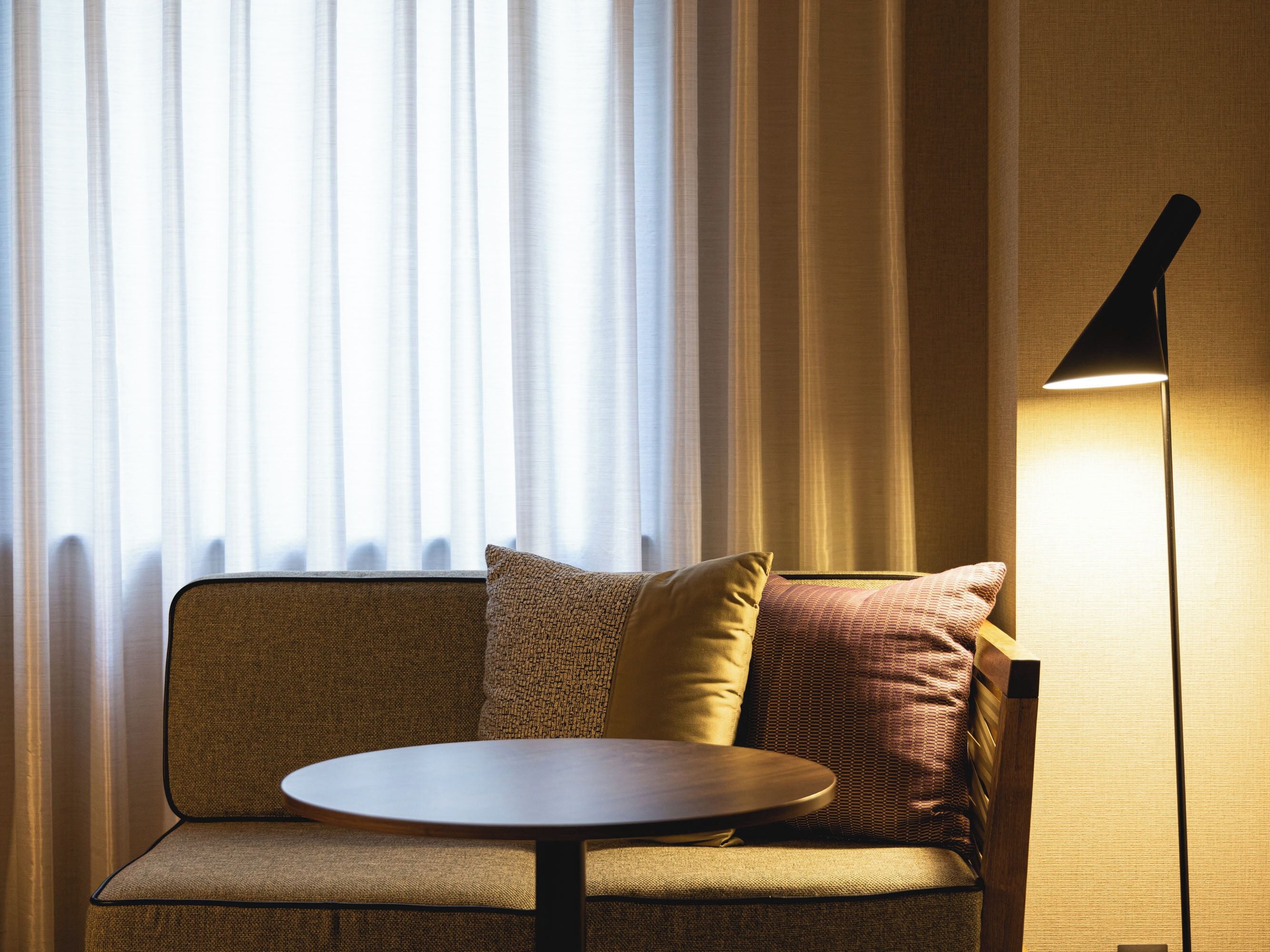 A sofa with a round table, a lamp, and sheer curtains in a room.