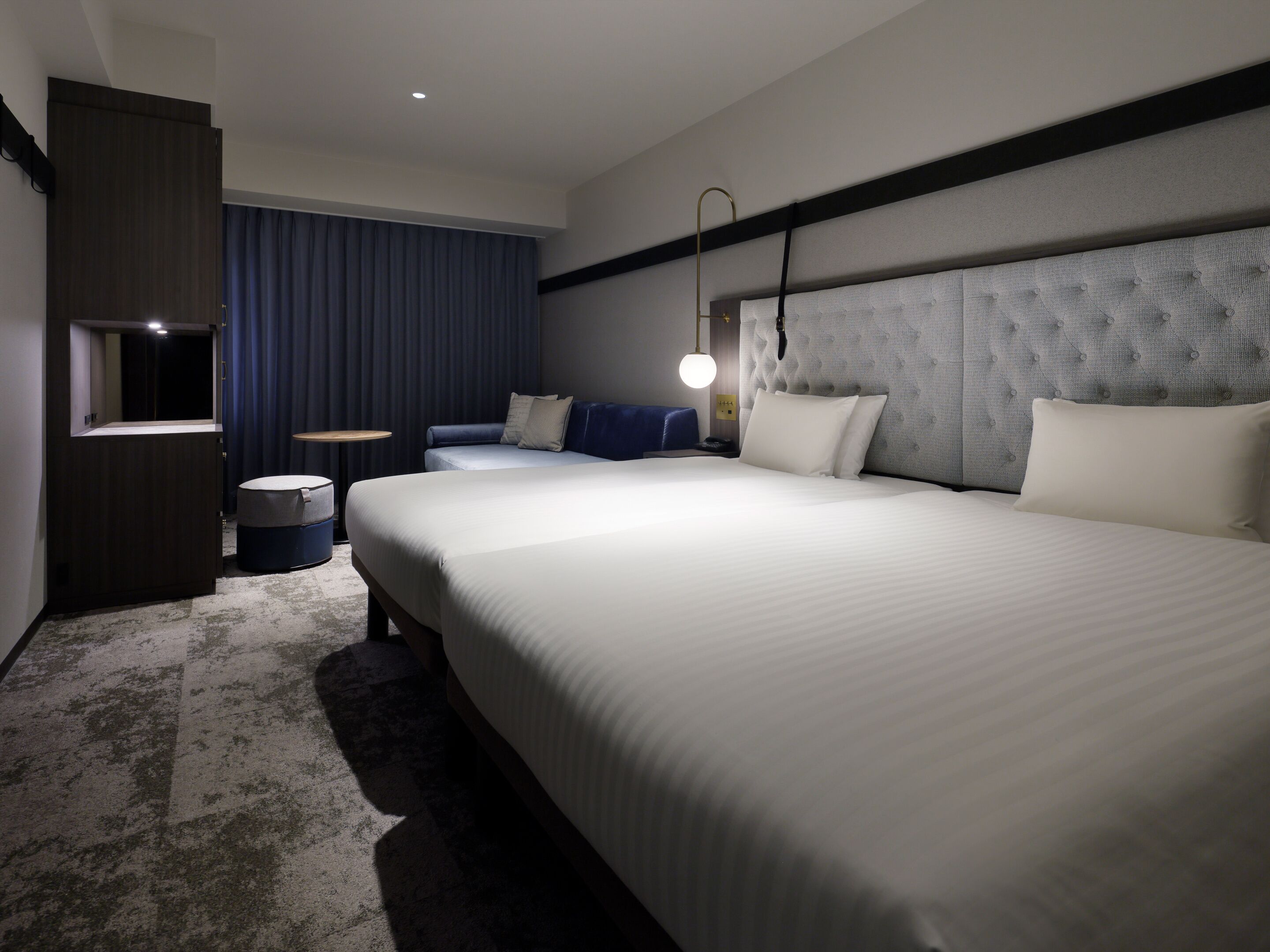 A hotel room with a large bed, a smaller seating area, a desk, and a window with curtains.