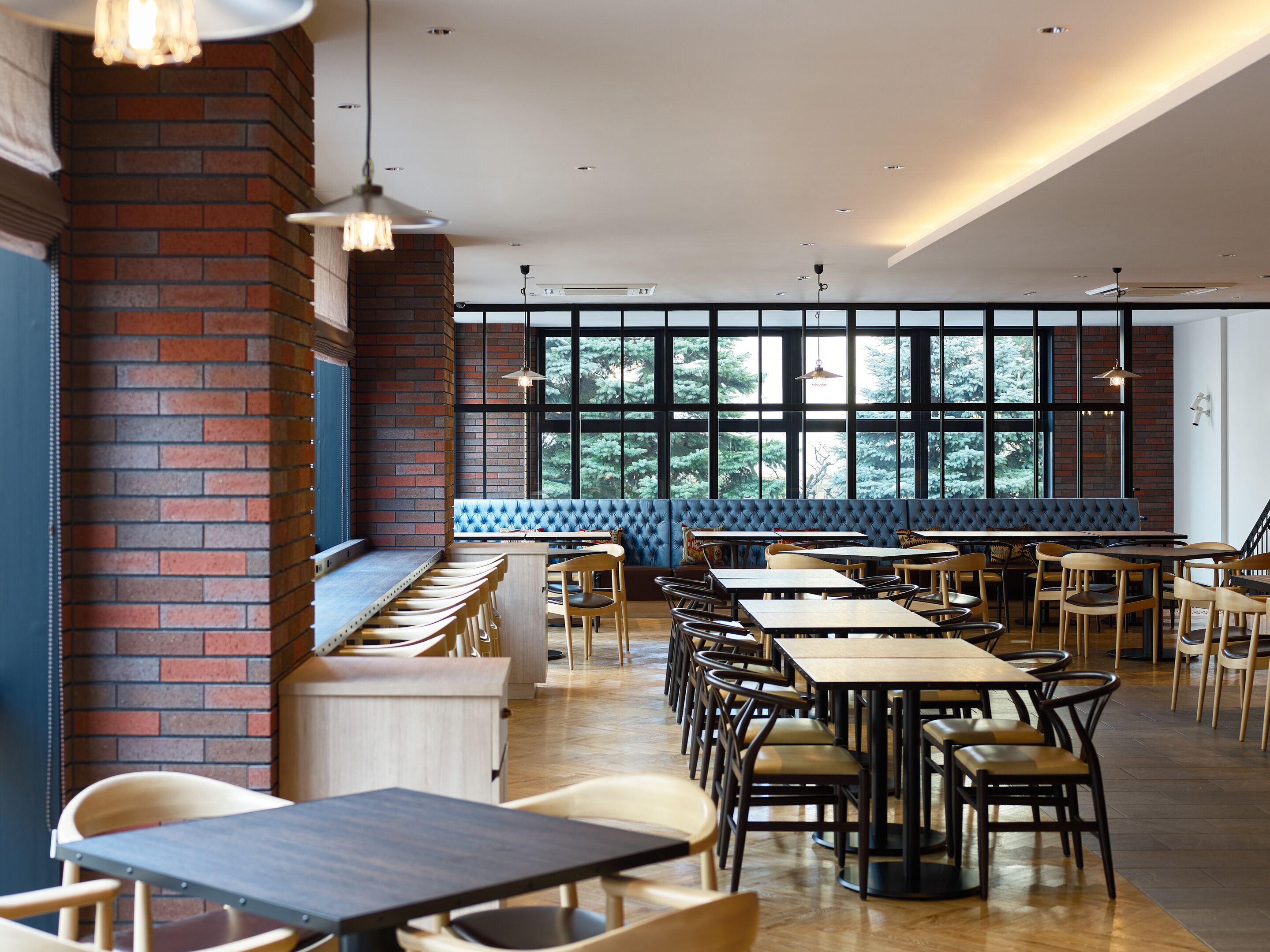 A restaurant with a long counter, multiple tables, and chairs. There is a large window with a view of trees.