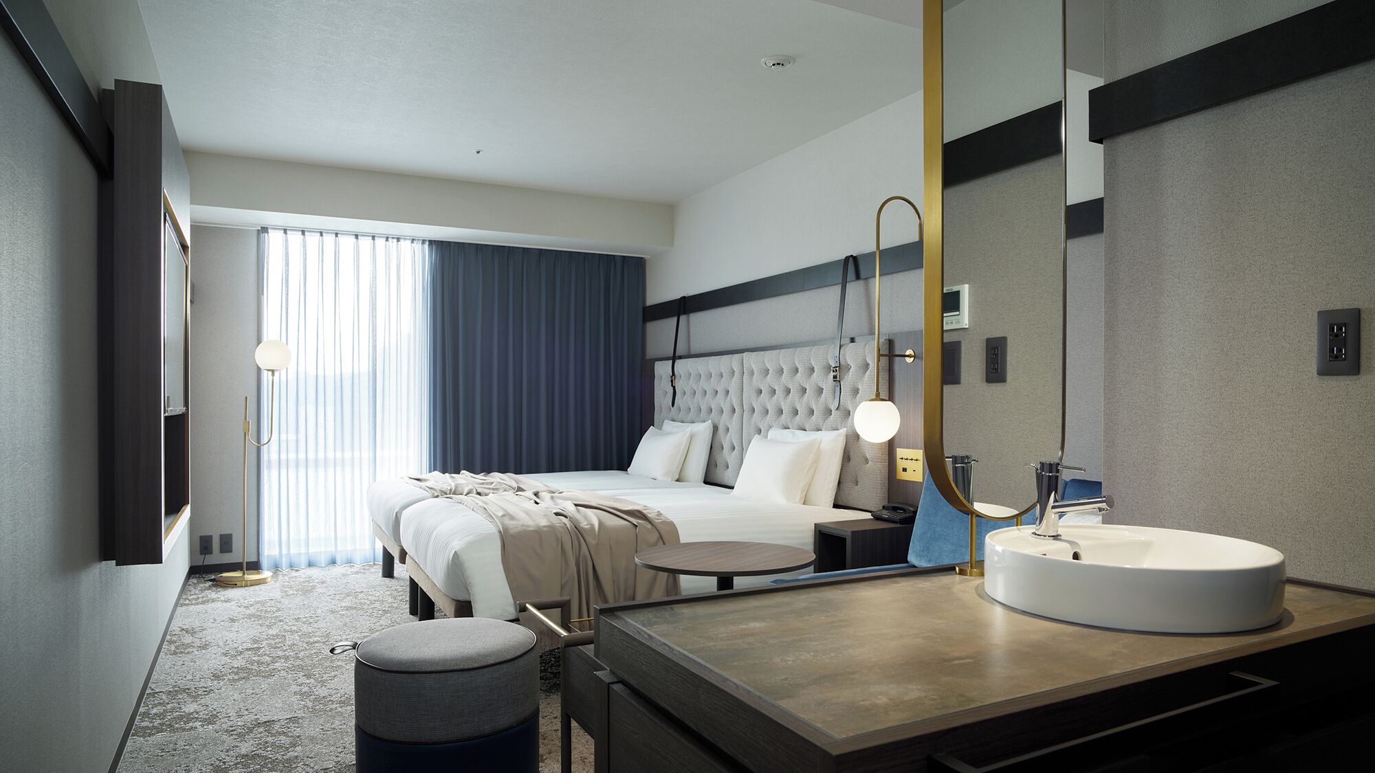 A modern hotel room with a bed, bedside table, round mirror, and a round sink.