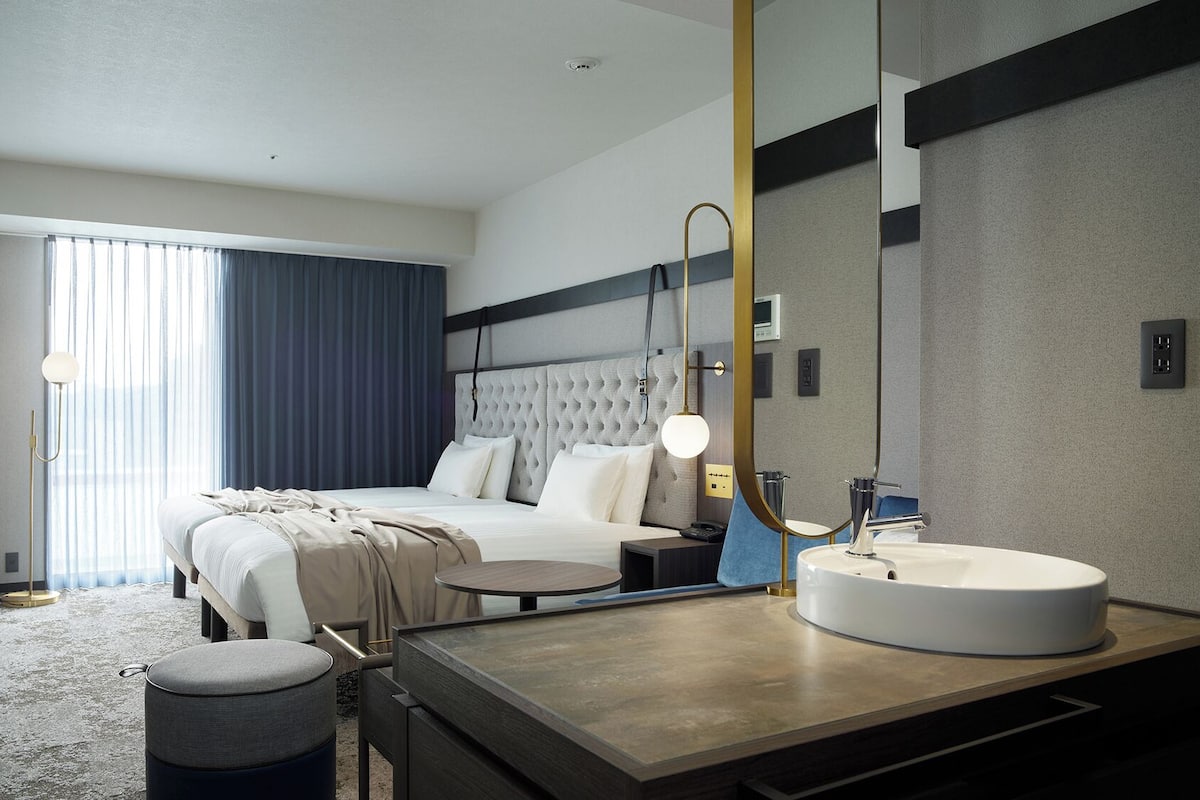 Ein modernes Hotelzimmer mit einem Bett, einem Nachttisch, einem runden Spiegel und einem Waschbecken.