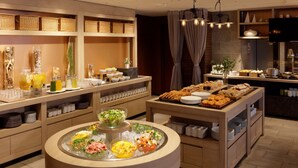 Un buffet proposant une variété de plats et de boissons, notamment des salades, des fruits et des pâtisseries, disposés sur des tables et des étagères en bois.