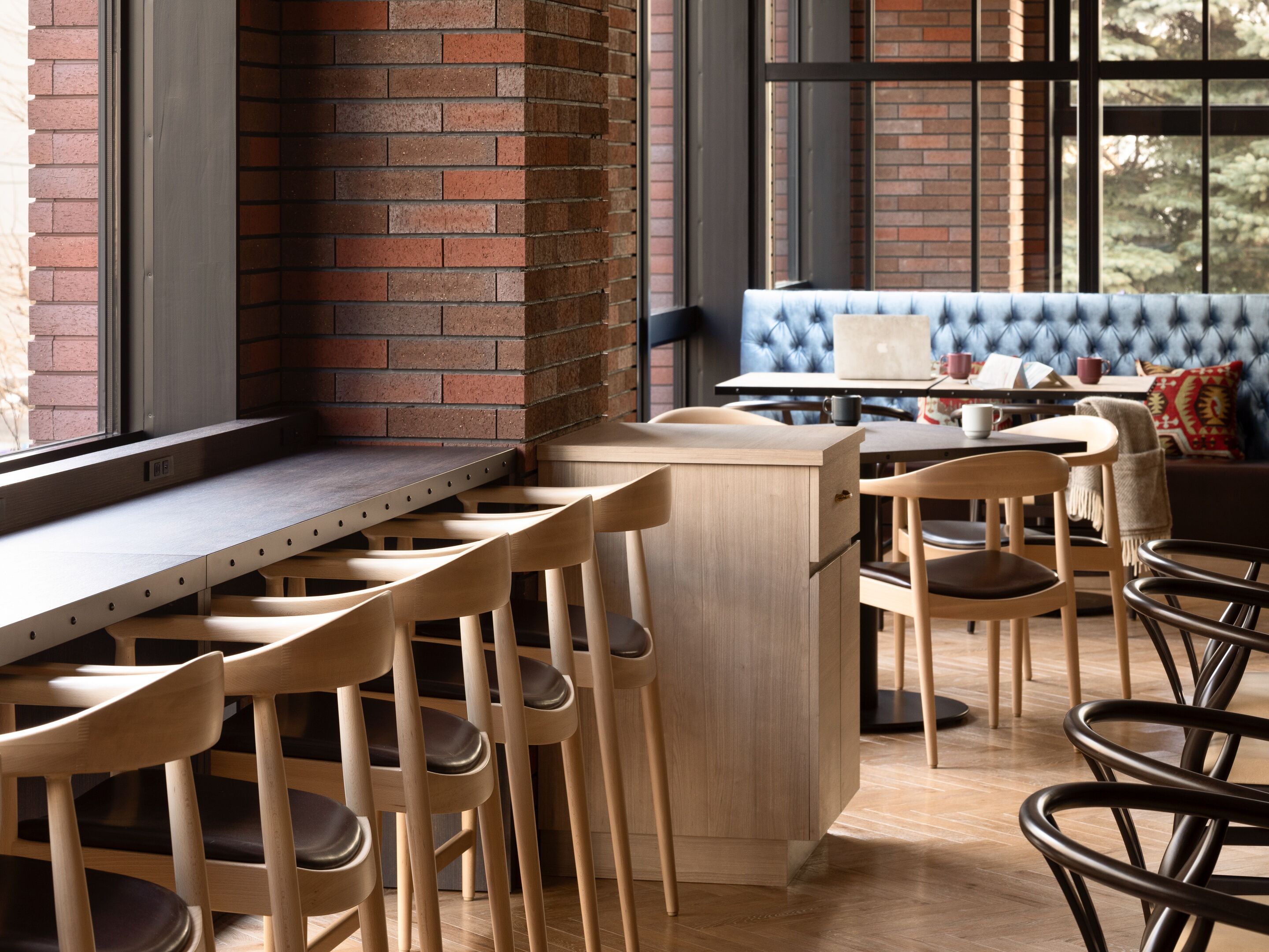 A modern kitchen with a brick wall, wooden bar stools, and a blue upholstered bench.