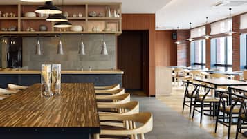 Un restaurant moderne avec une longue table en bois, de nombreuses chaises, des luminaires suspendus et un mur en briques.