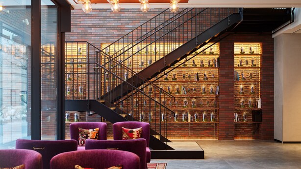 A modern interior with a staircase, purple armchairs, and a brick wall with shelves.