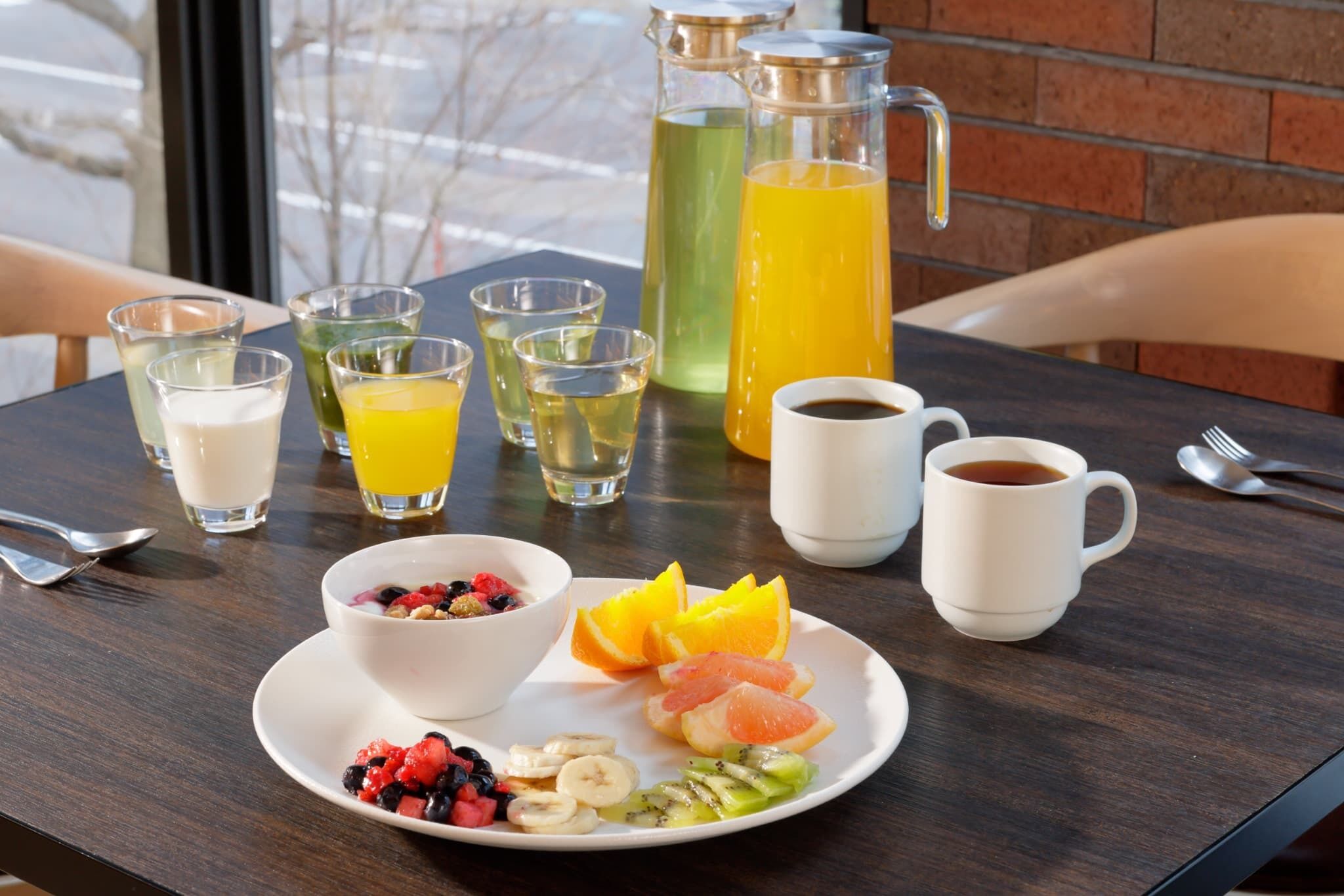 A breakfast setting with a variety of drinks, including juice and coffee, and a plate of fruit and cereal.