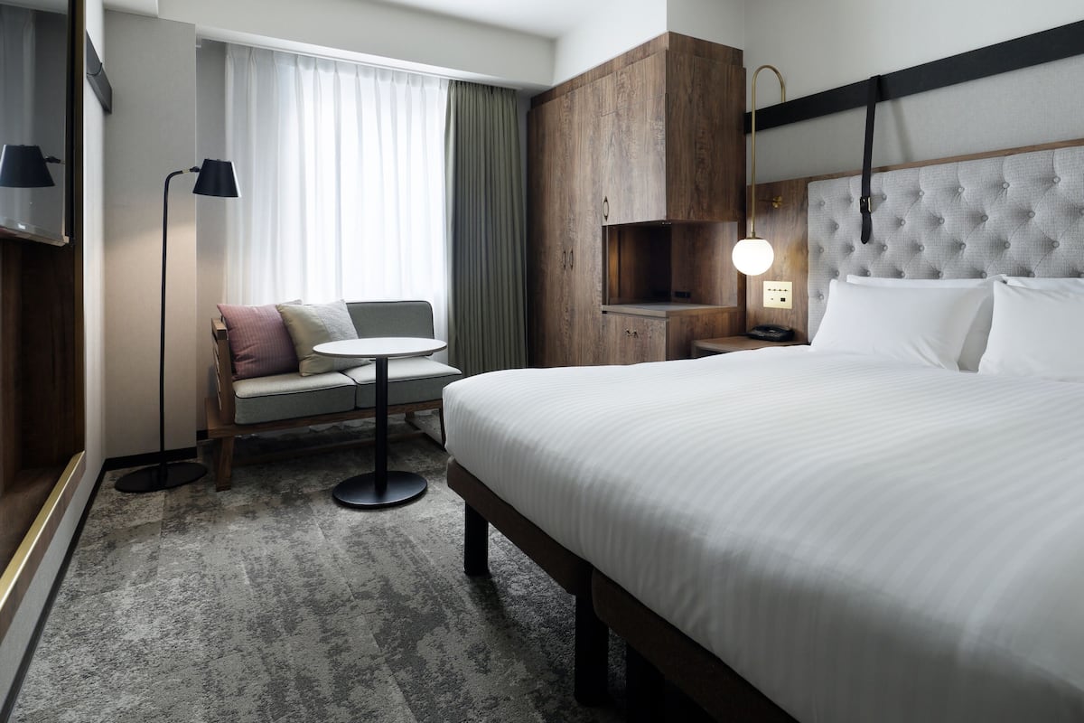 Une chambre d’hôtel comprenant un lit, un canapé, une petite table, un bureau, une lampe et une armoire.