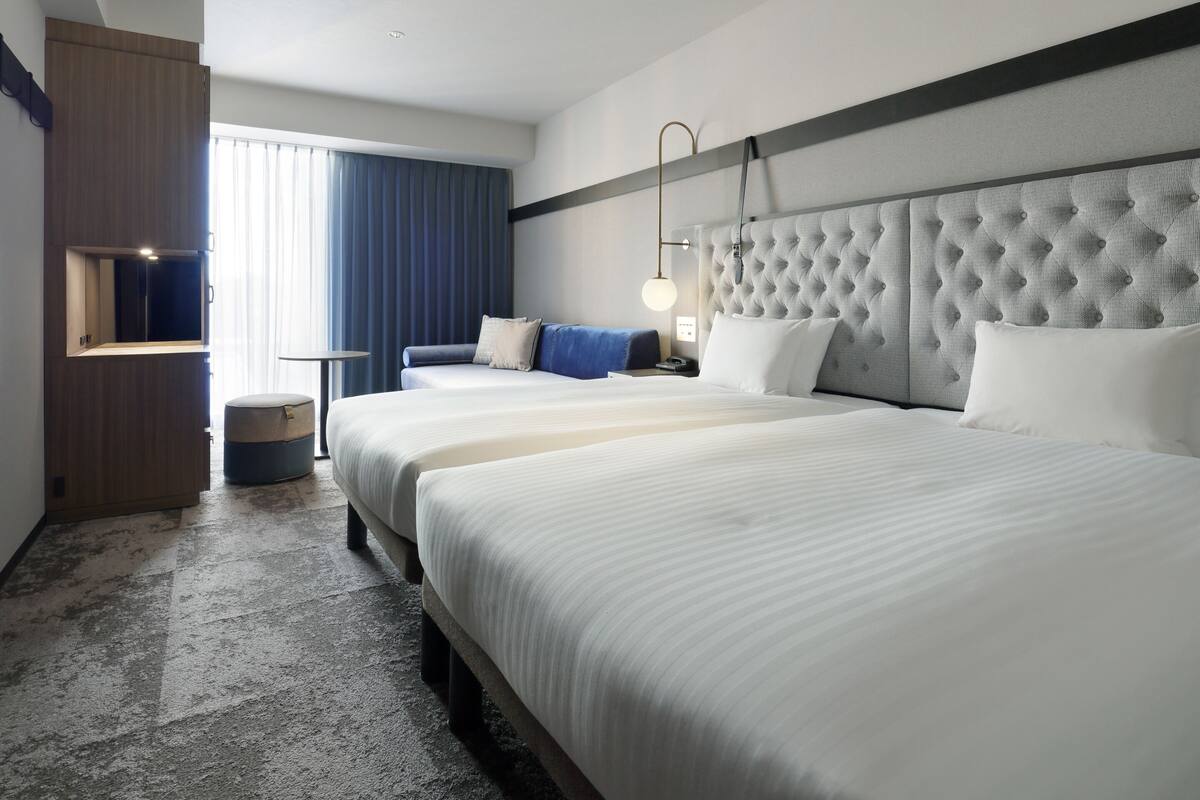 Une chambre d’hôtel avec un grand lit, une table de chevet, une chaise, une armoire et une fenêtre avec des rideaux.