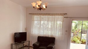 A living room with a television on a glass table, a black leather sofa, and a wooden coffee table. - Anba's (Trou aux Biches)