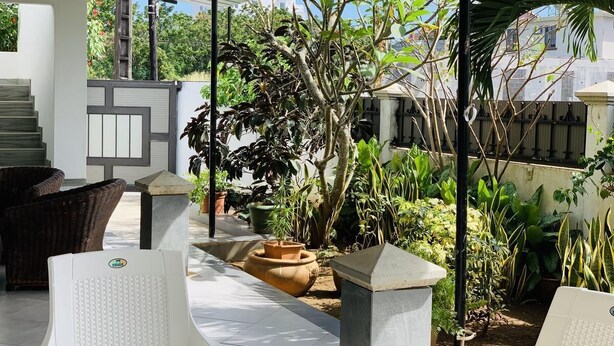 A covered outdoor area with wicker chairs, a potted plant, and a stone planter. - Anba's (Trou aux Biches)