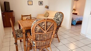 A dining area with a wooden table and chairs, a television on a stand, and a sofa with cushions. - Anba's (Trou aux Biches)