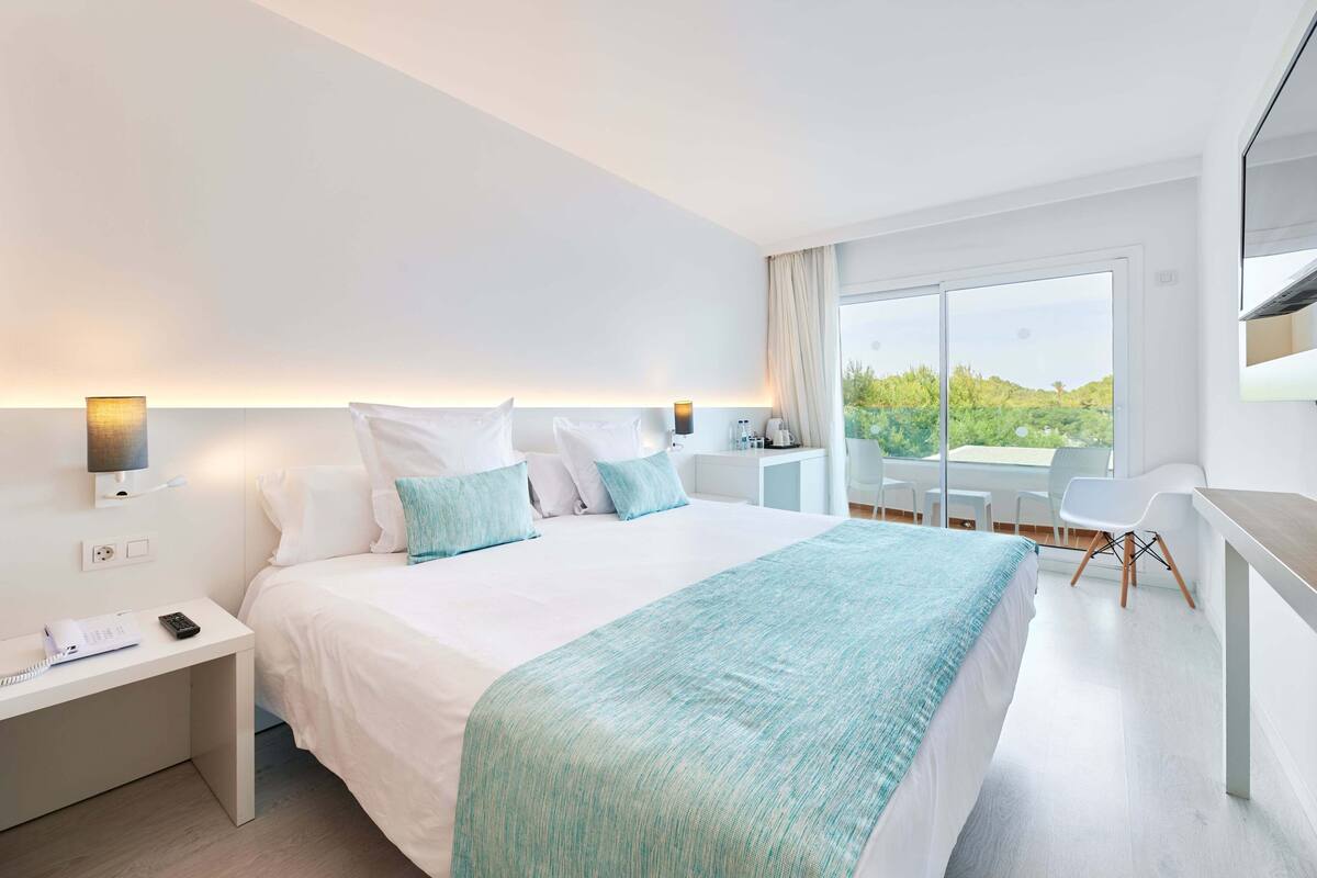 A modern hotel room with a large bed, bedside tables, a desk, and a balcony with a view.