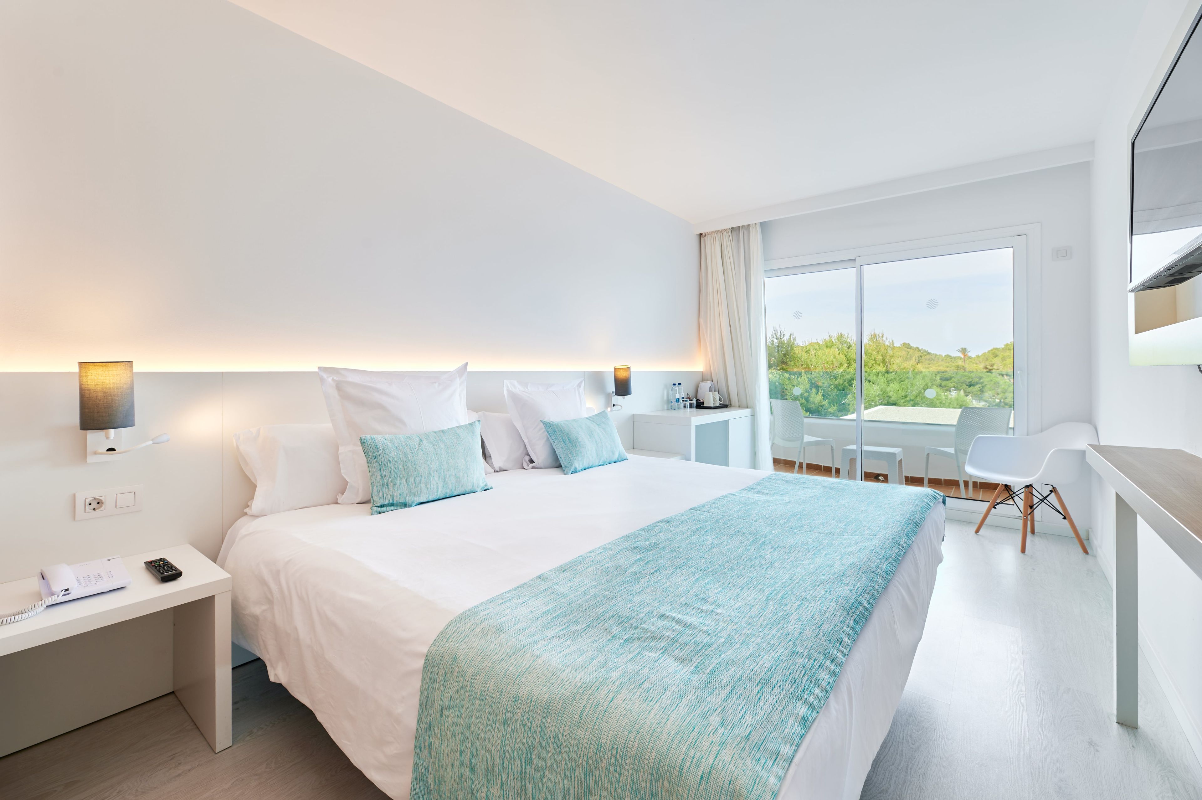 A modern hotel room with a large bed, bedside tables, a desk, and a balcony with a view.