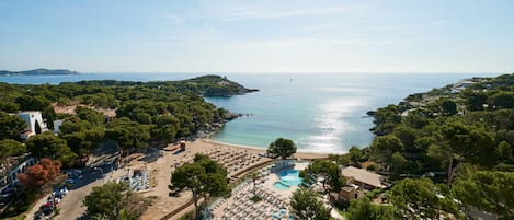 Vista aérea de un complejo turístico costero con piscina, playa y abundante vegetación.