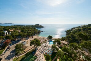 An aerial view of a coastal resort with a swimming pool, beach, and lush greenery. - Aluasoul Hotel Carolina (Capdepera)