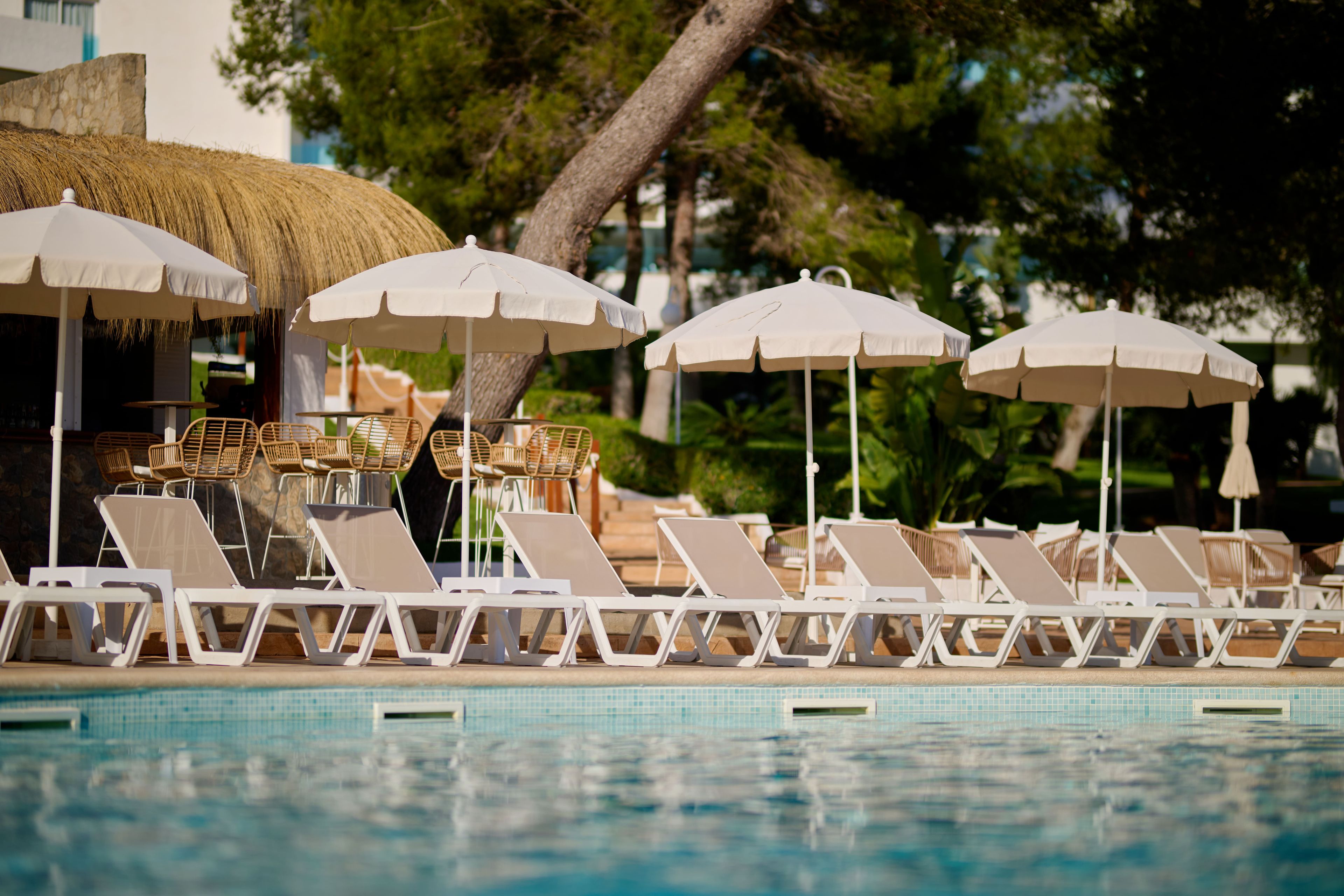 Un área junto a la piscina con sillones de descanso y sombrillas.