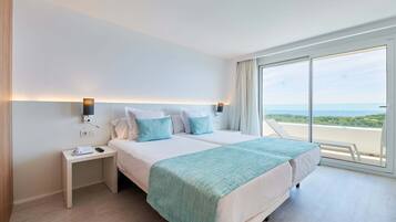 A modern hotel room with a large bed, a bedside table with a phone, and a view of the sea through large windows.