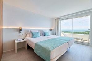 A modern hotel room with a large bed, a bedside table with a phone, and a view of the sea through large windows. - Aluasoul Hotel Carolina (Capdepera)
