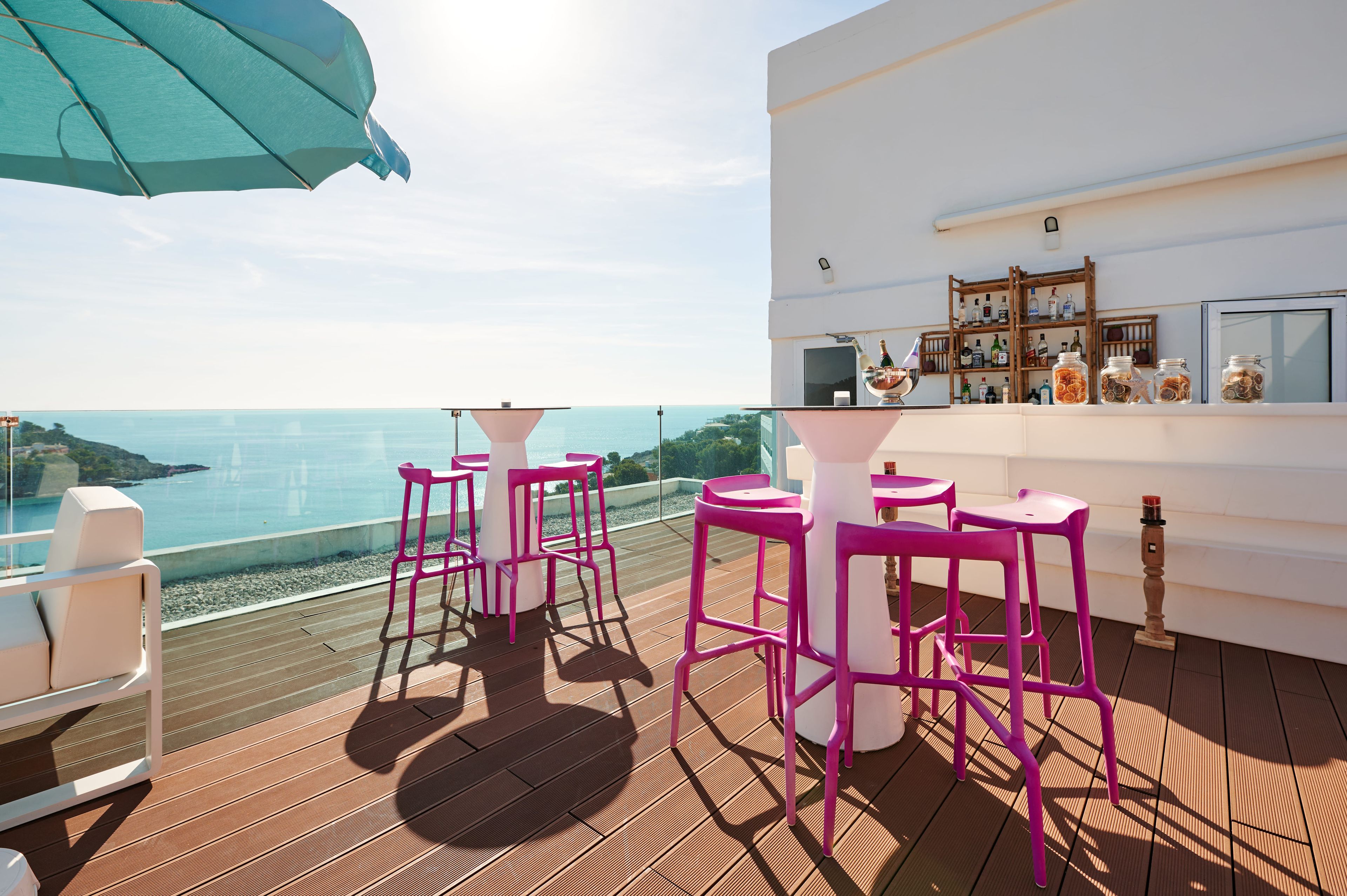 A deck with pink bar stools and a table, overlooking a body of water.