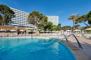 A swimming pool with lounge chairs and umbrellas, surrounded by trees and a hotel building. - Aluasoul Hotel Carolina (Capdepera)
