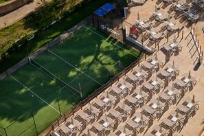 An aerial view of a tennis court surrounded by sun loungers and umbrellas, with a small building adjacent to the court. - Aluasoul Hotel Carolina (Capdepera)