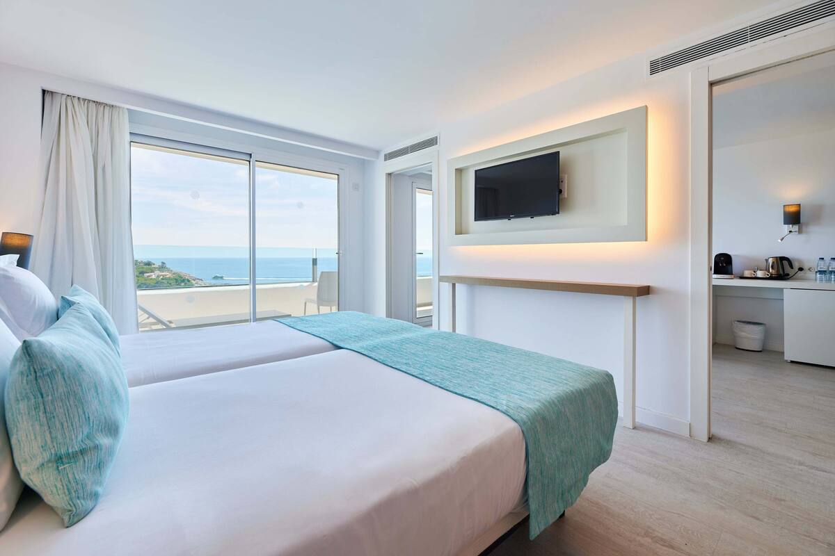 A hotel room with a large bed, a TV mounted on the wall, and a view of the sea.