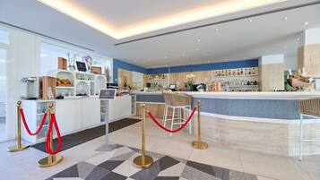 A modern hotel lobby with a reception desk, bar area, and a seating area.