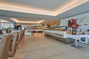 A modern restaurant with a long counter, multiple tables, and a kitchen area in the background. - Aluasoul Hotel Carolina (Capdepera)