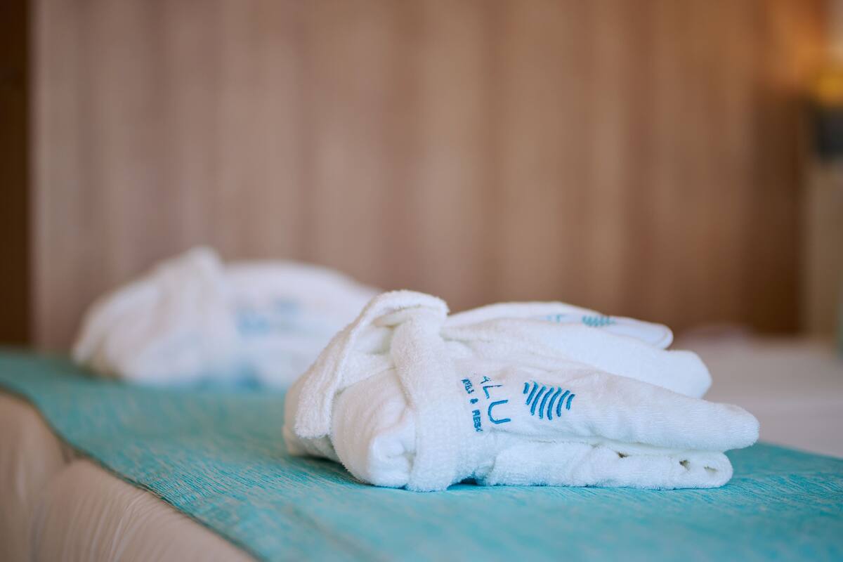 A neatly folded white towel with blue text on a teal-colored bedspread.