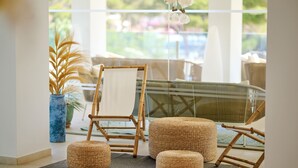 A room with a large window, a wicker chair, a small table, and a potted plant. - Aluasoul Hotel Carolina (Capdepera)